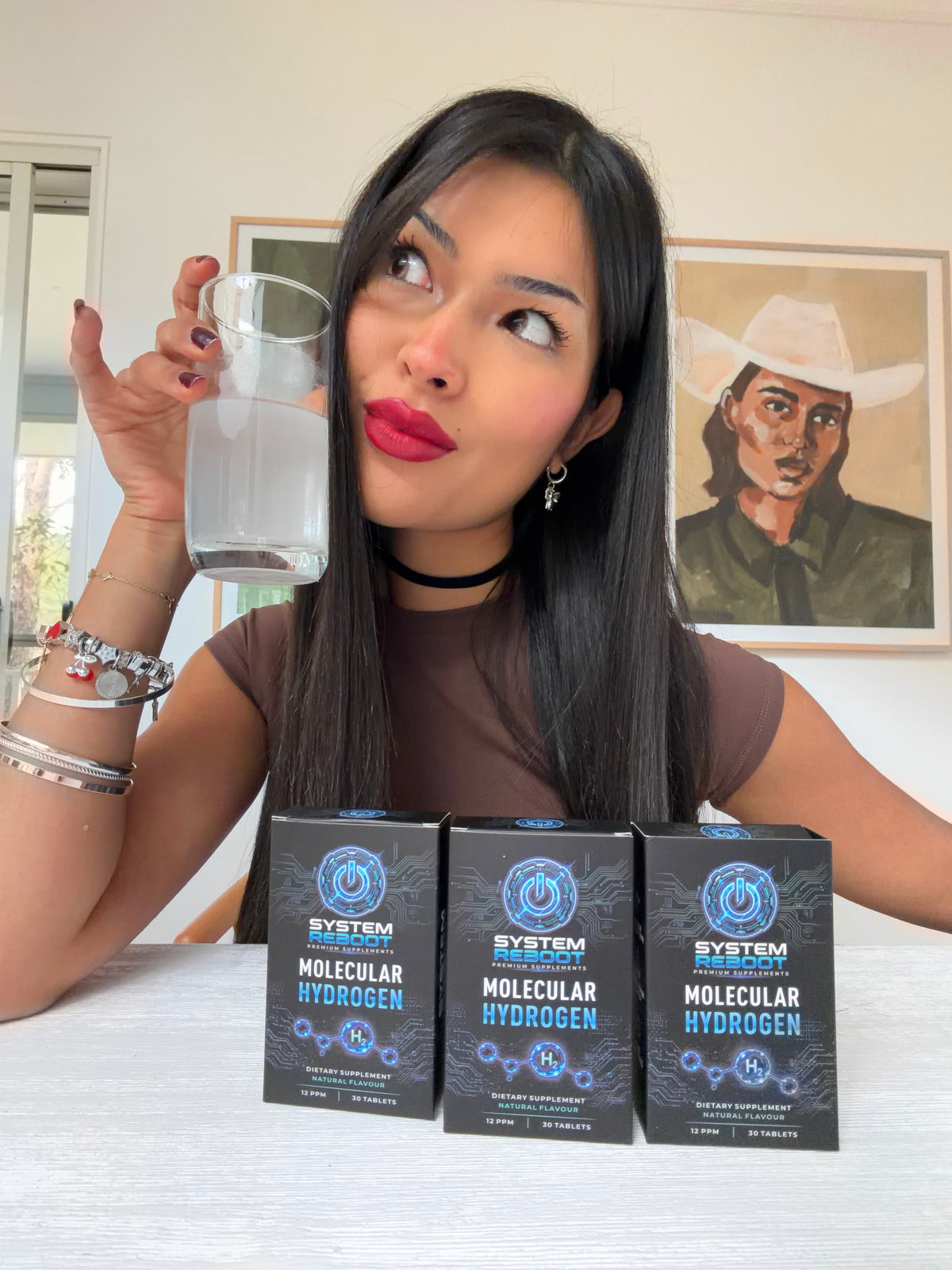 Bianca with a glass of hydrogen water and 3 boxes of System Reboot Molecular Hydrogen Tablets